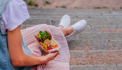 Young hipster girl holding lunch box sitting on stairs outdoor