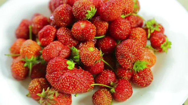 Strawberries lie on a white plate and rotate counter-clockwise. Loop