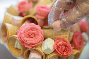 Hand of the confectioner in a polyethylene glove decorates the bouquet of roses and sweets