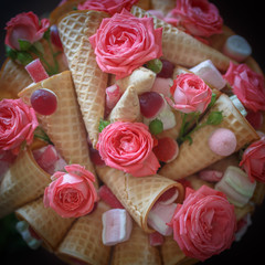 Bouquet consisting of flowers of pink roses, waffle cones, sweets and marshmallows on a dark background