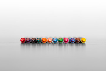 Row of twelve different colorful wax crayons from the front sharp point on black and white background. Creativity, imagination concepts. Copy space