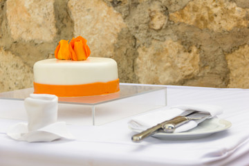 Wedding cake with orange flowers on top and service on white tablecloth. Bride and groom ceremony event dessert concept