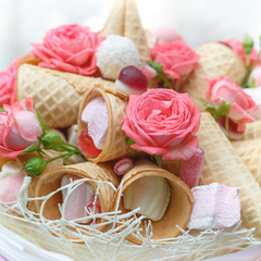 Obraz na płótnie Canvas Candies, marshmallows, pastille, waffle cones and natural pink roses are decorated in the form of a bouquet