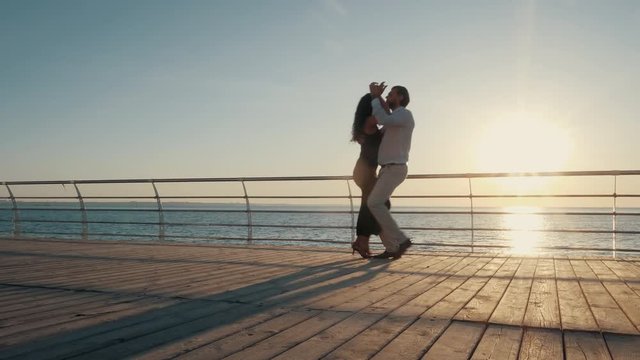 Dance latina performed by a professional couple on ocean beach. Woman in sexual black dress. Sensual salsa, bachata, rumba. 4k