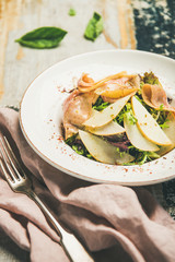 Fresh summer salad with smoked turkey ham and slices of pear in white plate over scorched rustic wooden table background, selective focus