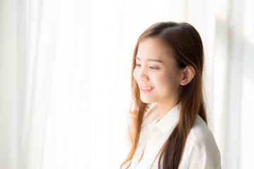 Portrait of beautiful young asian woman standing the window and smile while wake up with sunrise at morning, lifestyle and relax concept.