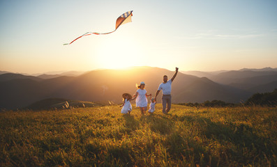 Fototapeta na wymiar Happy family father, mother and children launch kite on nature at sunset