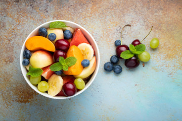 Bowl of healthy fresh fruit salad on a blue rusty background. Top view with copy space. Flat lay