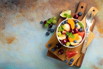 Bowl of healthy fresh fruit salad on a blue rusty background. Top view with copy space. Flat lay