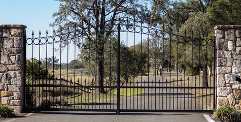 Metal driveway rural property entrance gates set in sandstone brick fence with eucalyptus gum trees in background