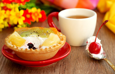 Tea and dessert in white and red colors. A cup of tea, a cake on a saucer and a red cherry berry on a dessert spoon. Tea and cake in the process of eating on the table.