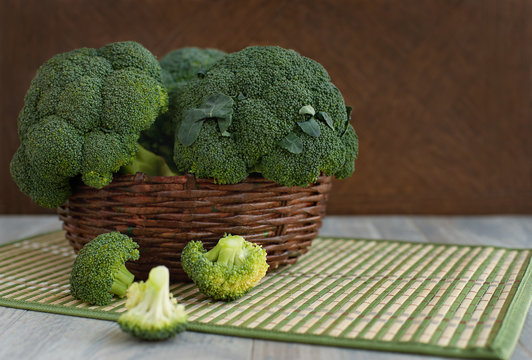 A large basket of broccoli. A lot of broccoli in the basket and a knife for cooking dishes. Sliced vegetables on a cutting board. Cabbage in a wicker box.