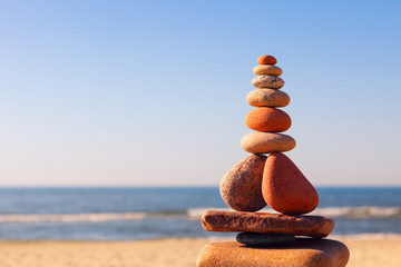 Rock zen pyramid of white and pink pebbles on a background of blue sky and sea.