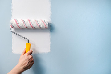 A hand with a roller paints the wall with white paint