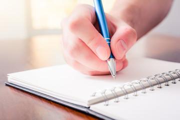Front View Of A Male Hand Writing With A Pen In A Blank Book In Front Of A Bright Background