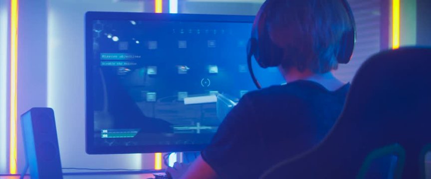 Pro Gamer Plays in the First Person Shooter on His Personal Computer. Talks with Teammates through Headphones. Neon Colored Room. Online eSport Tournament in Action. Shot on Anamorphic Lens.