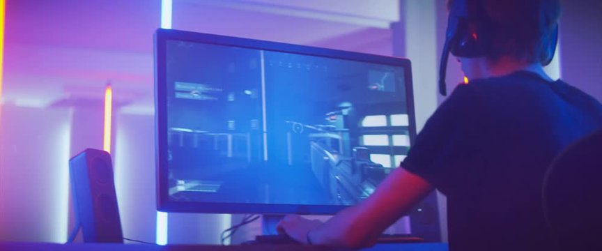 Pro Gamer Plays in the First Person Shooter on His Personal Computer. Talks with Teammates through Headphones. Neon Colored Room. Online eSport Tournament in Action. Shot on Anamorphic Lens.