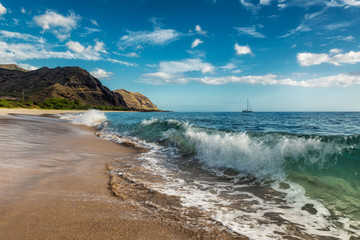 Makua beach view of the wave with beatiful mountains and a sailboat in the background, Oahu island, Hawaii