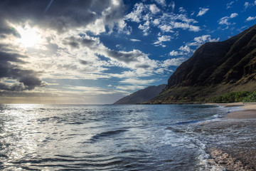 Sun shining through the clouds at sandy beach with waves