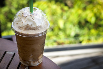 A glass of milk chocolate frappe with whipped cream for sweet and beverage on wooden table and...