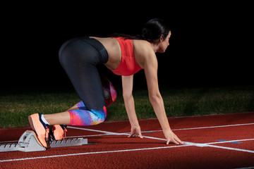 woman sprinter leaving starting blocks on the athletic track. exploding start on stadium with...