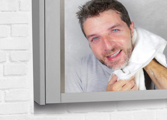 Fototapeta premium young happy attractive man using towel drying face after washing looking at the bathroom mirror smiling cheerful and positive feeling clean and fresh
