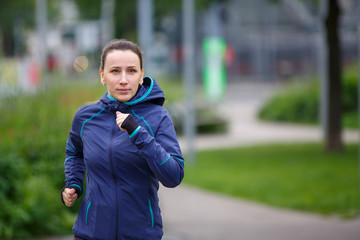 Young woman in blue jacket jogging in park. European girl running in the morning. Image vith copy space