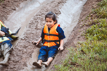 Cute asian child girl wearing life jacket having fun to play slider with muddy that make from...