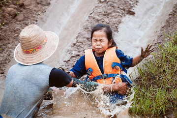 Cute asian child girl wearing life jacket having fun to play slider with muddy that make from nature in the rice field