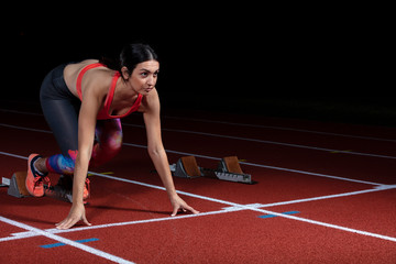 woman sprinter leaving starting blocks on the athletic track. exploding start on stadium with reflectors