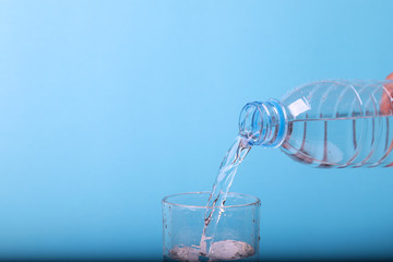 Closeup of pouring mineral water from bottle into glass with blue background. 