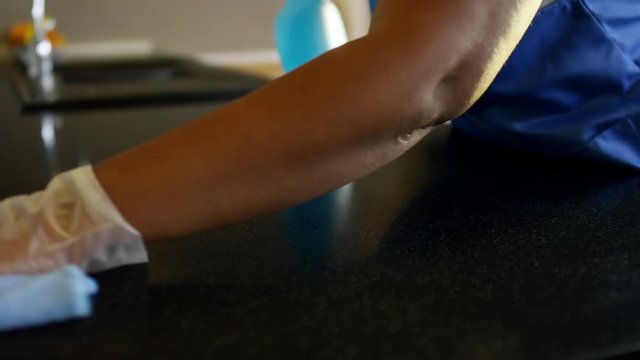 Close up of hands of unrecognizable black female housecleaner in gloves and uniform sanitizing kitchen counter in clients house