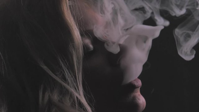 Attractive blonde girl in white thick smoke cloud, closeup portrait shot in slowmotion, dark background