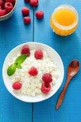 Fresh ricotta or curd cheese with raspberries and honey on blue wooden table, top view, healthy eating concept