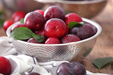 Strainer with ripe juicy plums on table