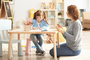 Female psychologist with cute little girl during art therapy