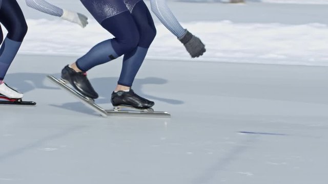 Front view of four professional athletes sprinting along track when practicing speed skating on ice rink in winter