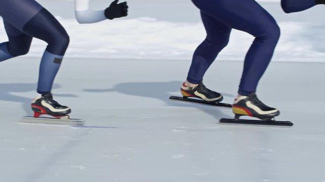Legs of four professional athletes wearing racing suits when skating along track on outdoor ice rink in winter
