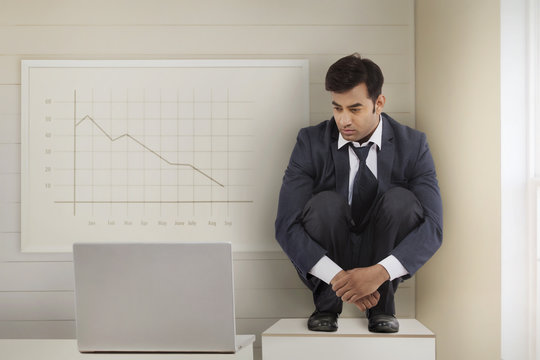 Confused businessman with laptop at whiteboard in office