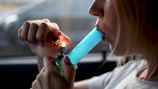 A woman smokes marijuana. The use of hashish through a bong in the car.