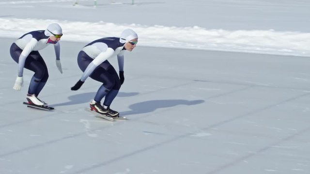 Two professional female athletes racing along track on outdoor ice rink when practicing speed skating in winter