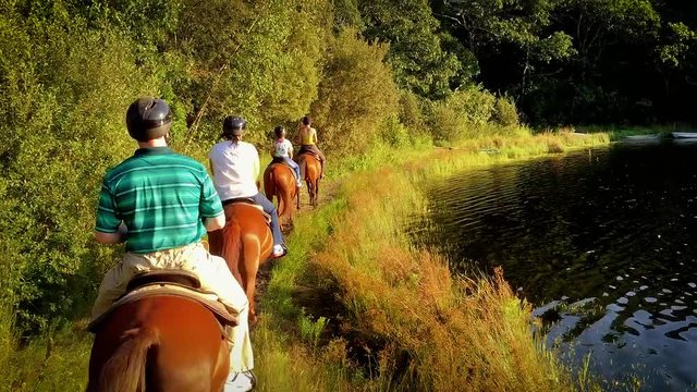A family rides horses along a lake.