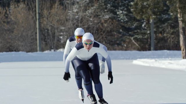 Locked down shot of two determined female speed skaters in sportswear racing along track on outdoor ice rink in winter