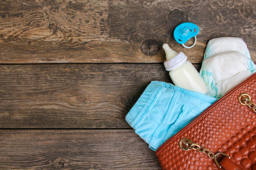 Women's handbag with items to care for the child on old wooden background