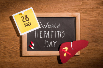 top view of blackboard with lettering world hepatitis day, liver, pills and stick it with lettering 28th july on table