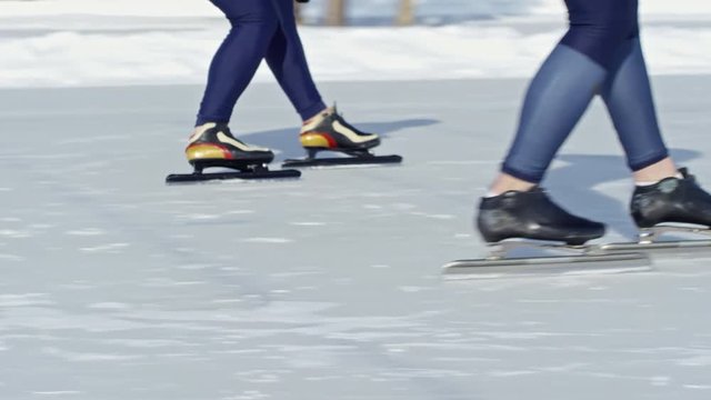 Legs of two unrecognizable athletes in sportswear practicing speed skating along track on outdoor ice rink in winter