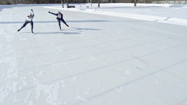 High angle view of two professional athletes in racing suits finishing competition in speed skating on outdoor ice rink