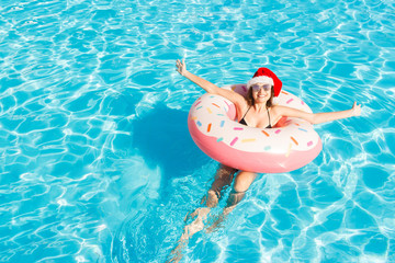 bikini girl in Santa Claus hat with sunglasses relaxed on pink inflatable pool ring. copy space