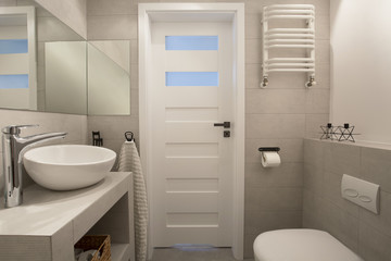 Mirror above washbasin in beige bathroom interior with toilet and door. Real photo