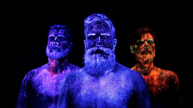 Three bearded men in UV powder are standing static